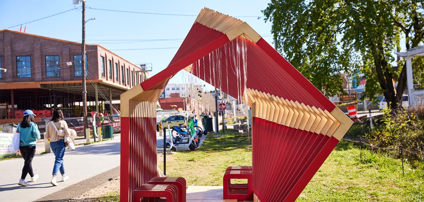 An art structure that resembles large popsicle sticks sits on the side of the Beltline, where people walk by.