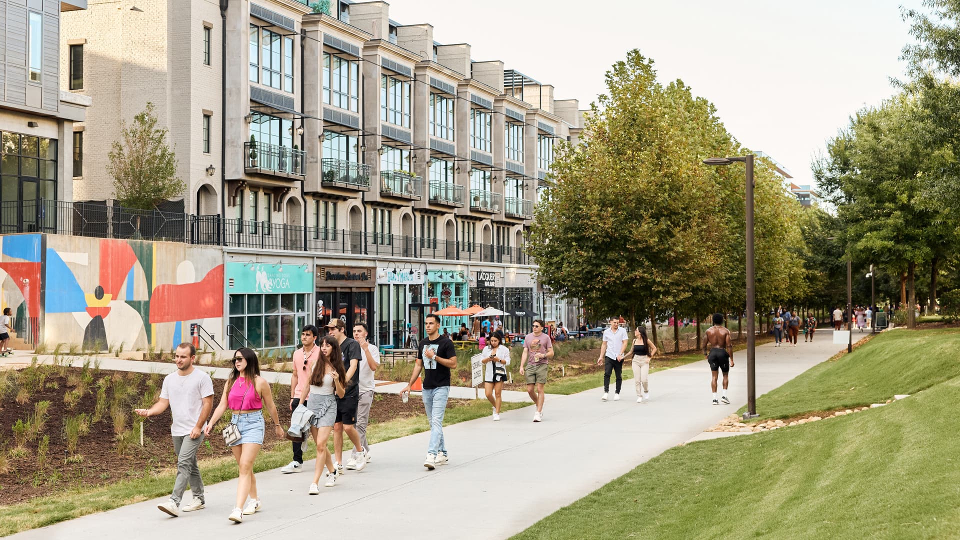 People walk along a trail surrounded by buildings and greenery.